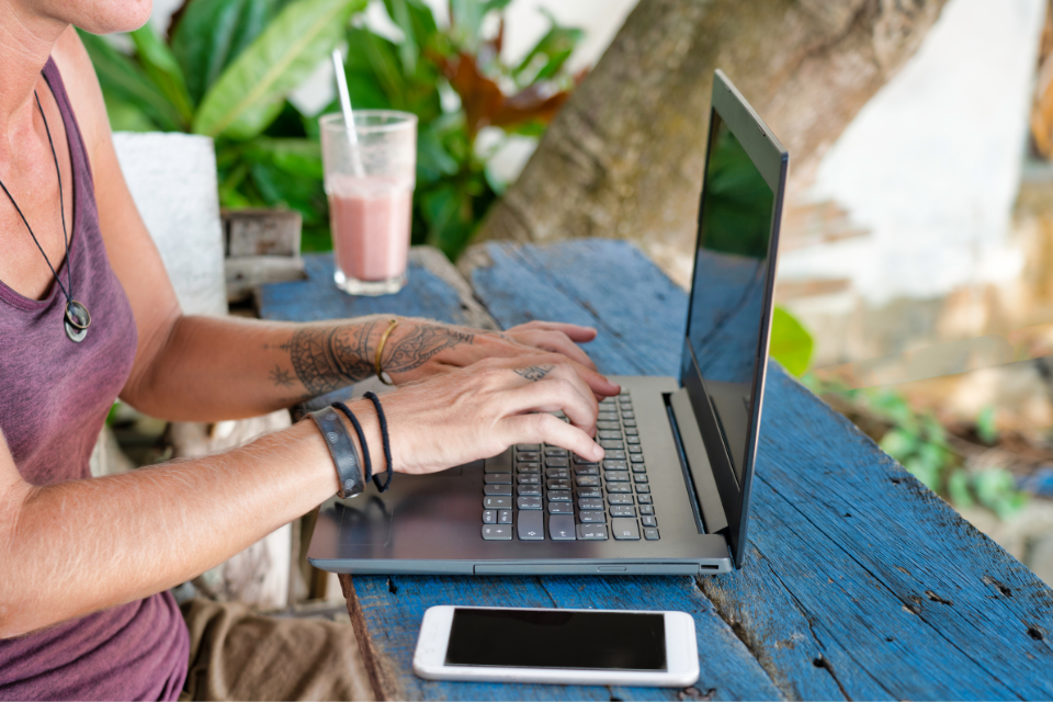 A woman sits at an outdoor workspace and types on her laptop