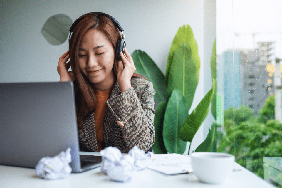A worker wears headphones while in front of her laptop
