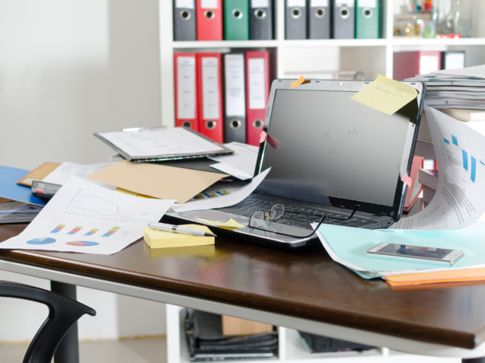 A desk cluttered with laptop and papers