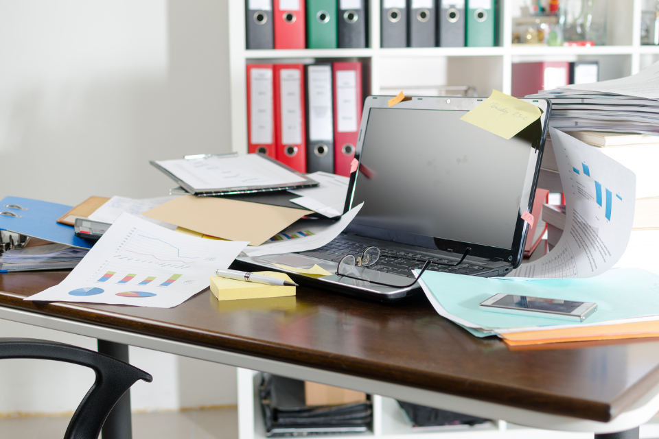 A desk cluttered with laptop and papers
