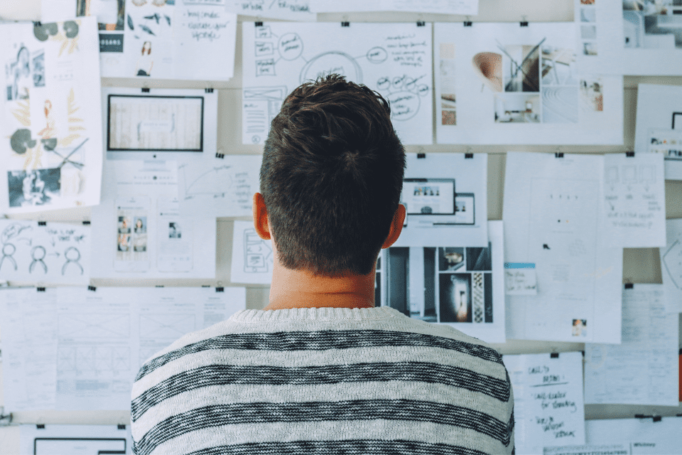 A man looks at a bulletin board pinned with many drawings and ideas