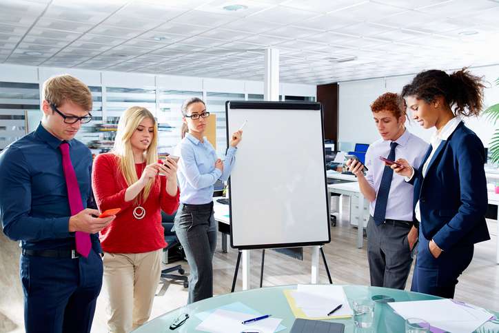 A team gathers around a whiteboard but everyone is distracted by their phones