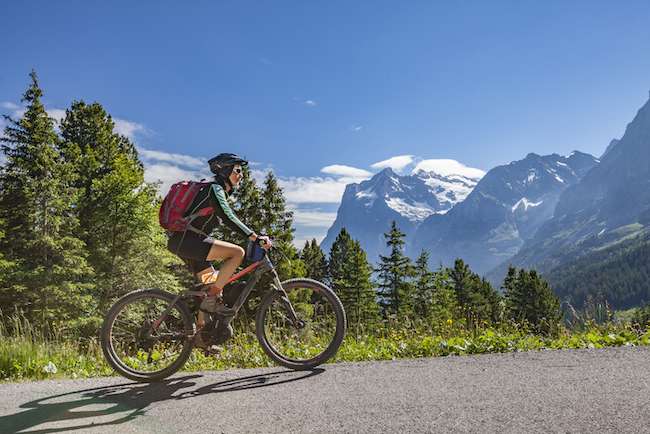 woman rides bike up road by mountain