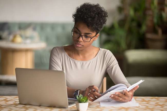 Focused student looking at laptop holding book doing research