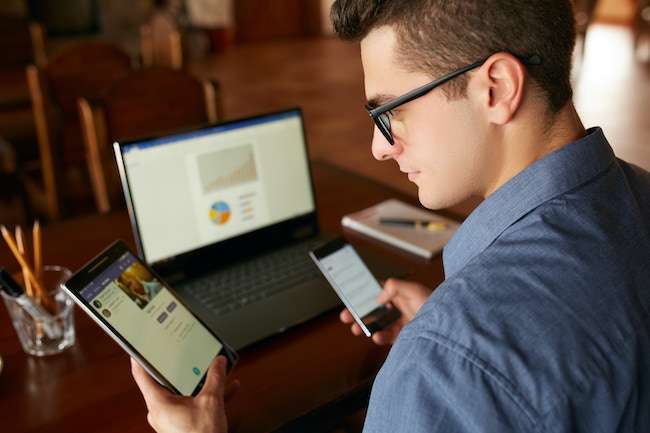 a man looks at phone, computer and tablet at same time
