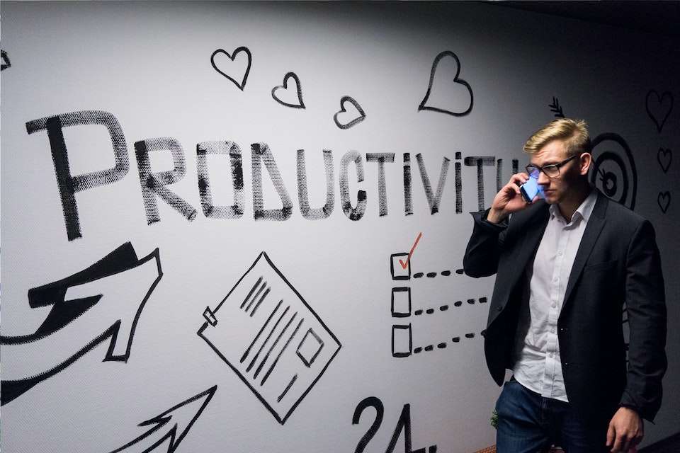 office worker drinks coffee while looking at a sign that says "Productivity"