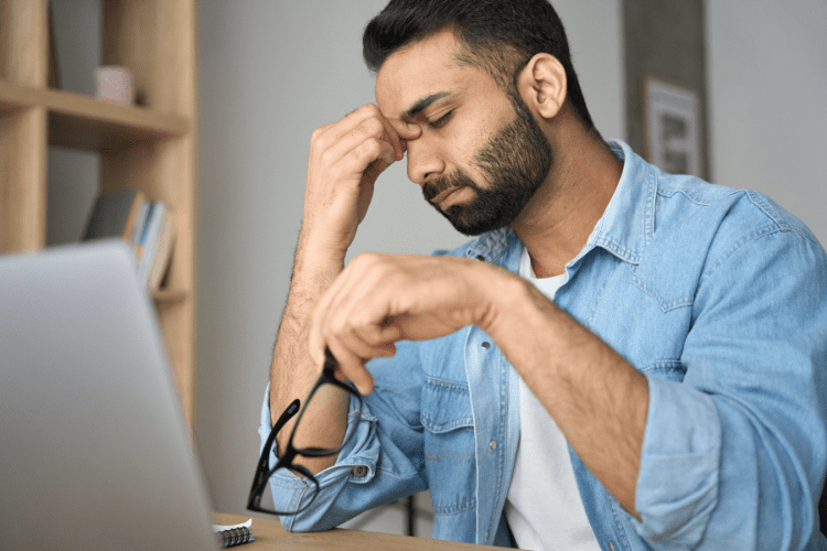 A man sits at his desk holding his head, overwhelmed by work