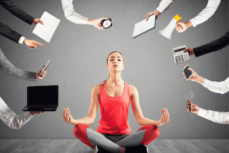 A woman in yoga clothes sits with her eyes closed surrounded by outstretched hands holding various communication tools like a bullhorn and a computer and a clock