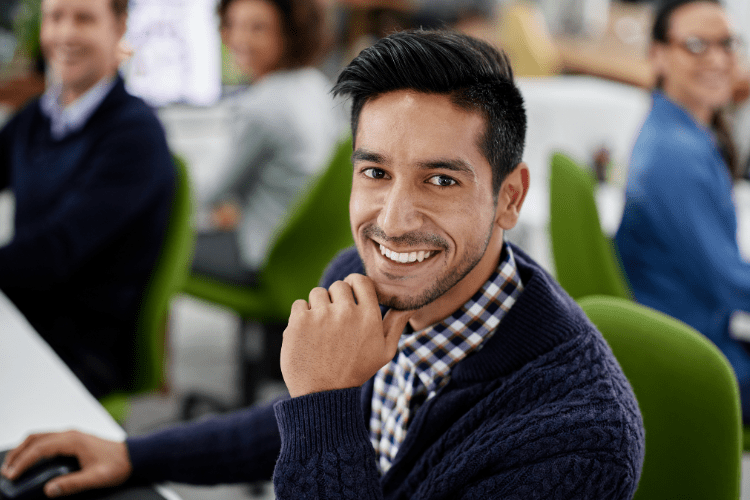 A young worker is smiling at his office desk