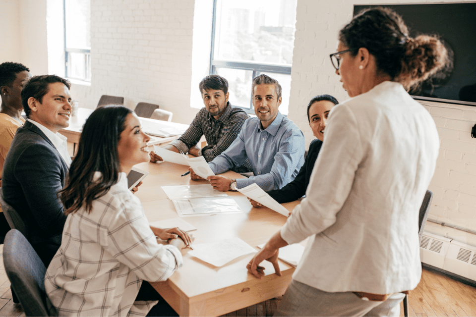 A woman stands at the head of a table leading a meeting