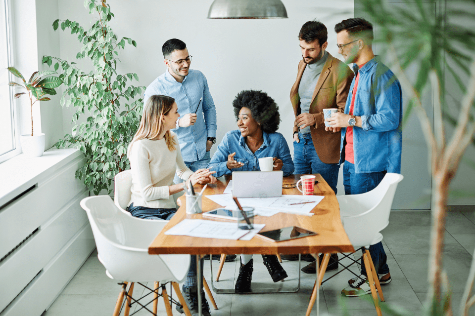 A leader sits at a table and works with team members who stand around