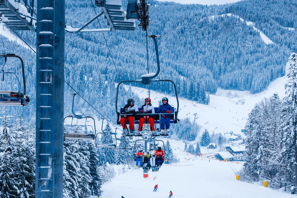 3 people riding the lift up a ski mountain while on vacation
