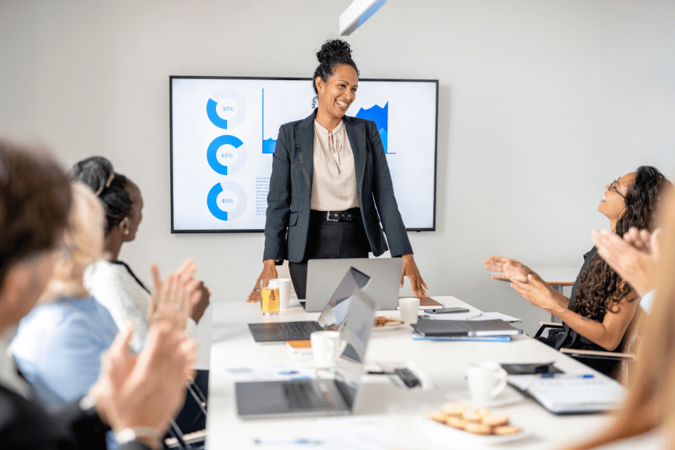 corporate trainer stands at the head of a conference table with employees seated around it