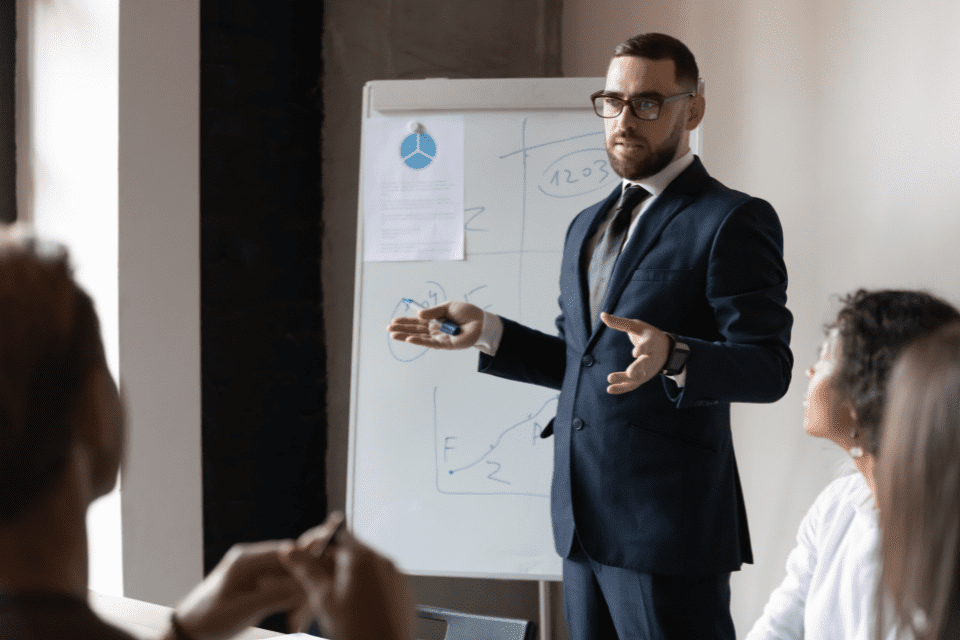 A learning and development professional stands at a flip chart and provides training to a team in a corporate conference room