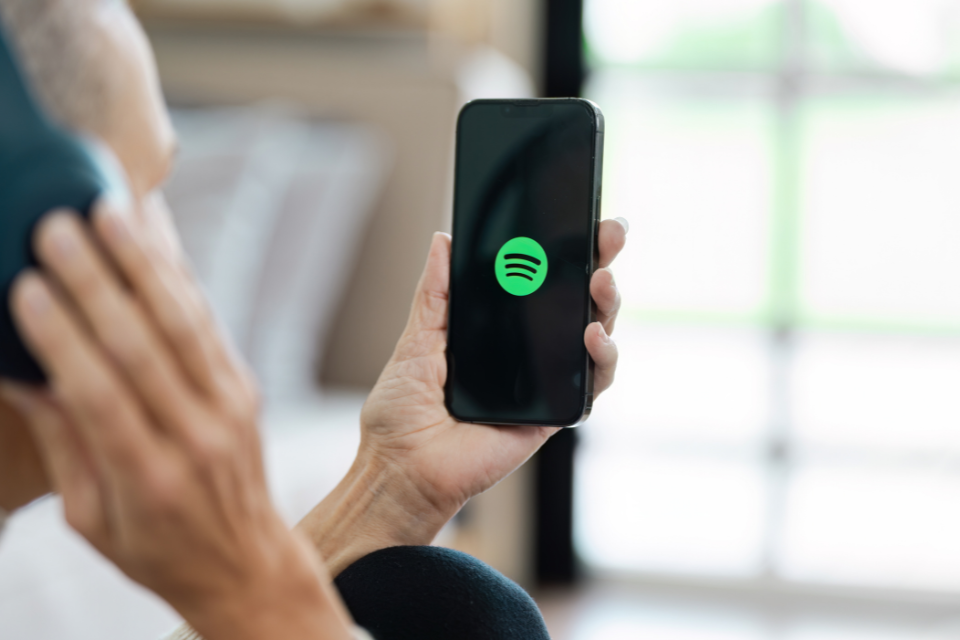 Man with headphones holds iPhone with spotify app open