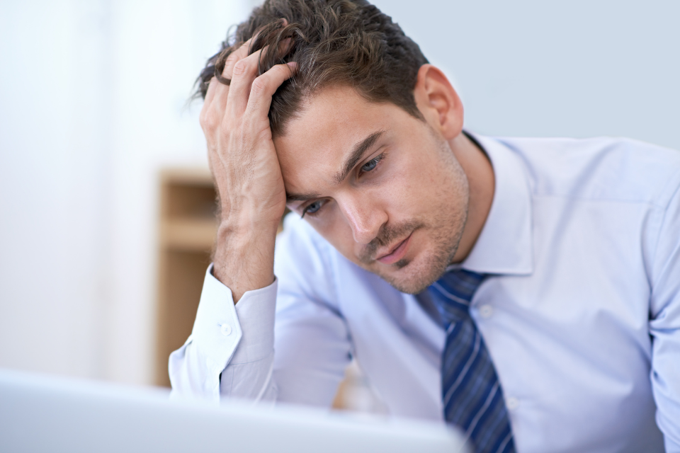 A man sits at desk with hand to head, overwhelmed