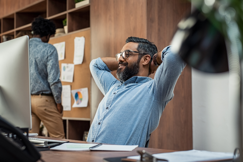 Man sits at desk at work and holds hands behind his head