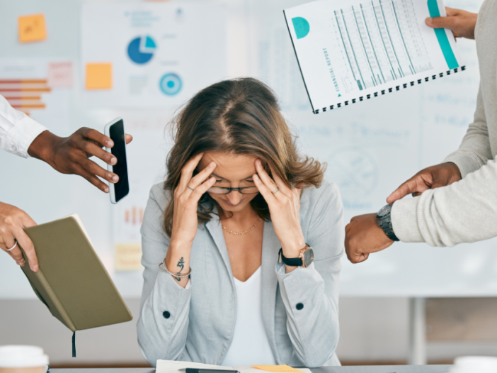 A woman with hands to her forehead while others are asking her to check the time and check their phone. She is overwhelmed.