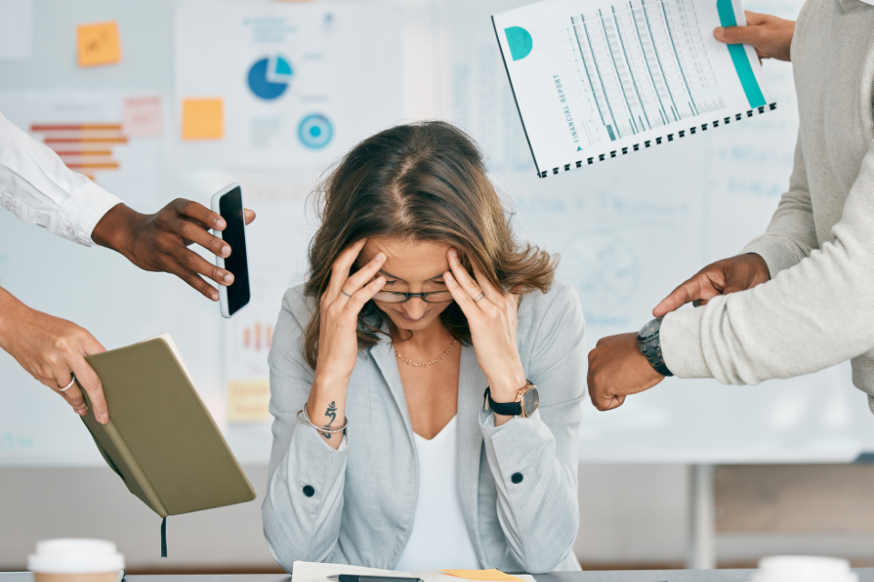 A woman with hands to her forehead while others are asking her to check the time and check their phone. She is overwhelmed.