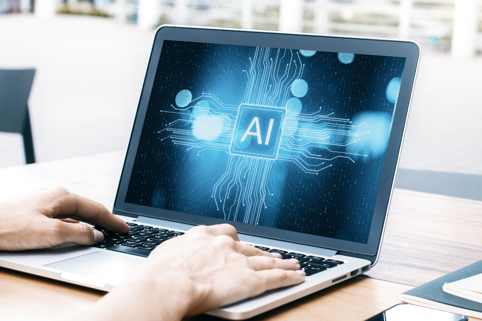 Human hands on a laptop keyboard. The letters "AI" are written on the laptop screen.