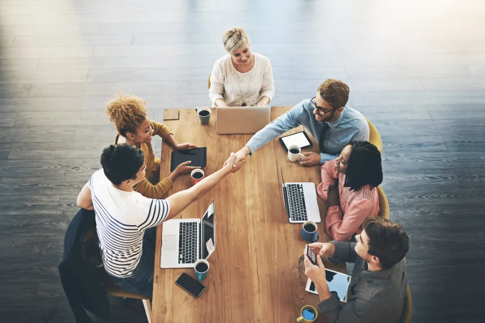 Aerial view of a well organized team sitting around conference table. Two team members shake hands across the table.