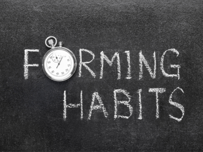 A chalkboard with the words "Forming Habits" written on it. The letter 'o' in the word 'forming' is replaced with a circular stopwatch.