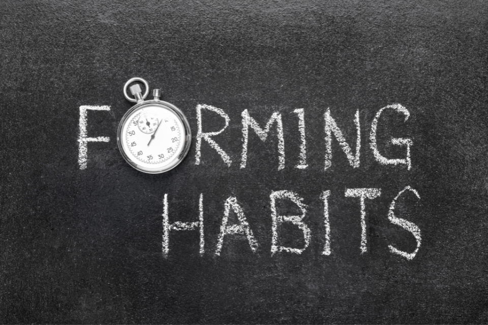 A chalkboard with the words "Forming Habits" written on it. The letter 'o' in the word 'forming' is replaced with a circular stopwatch.