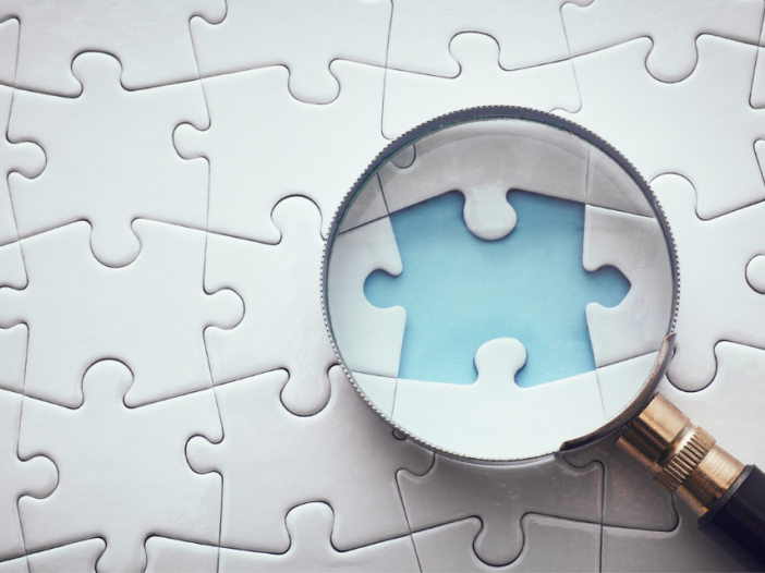 A magnifying glass on top of a puzzle showcases one missing piece