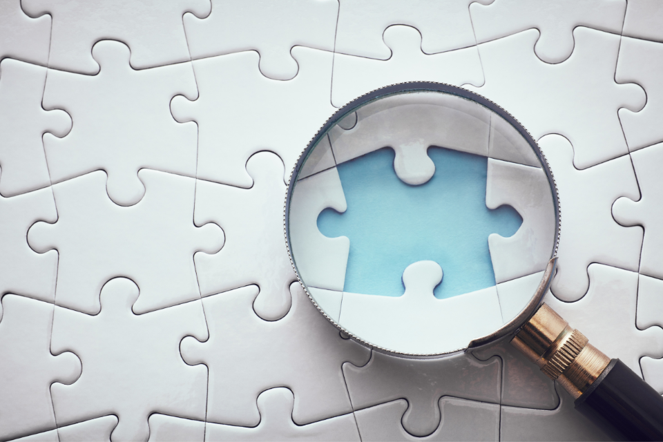A magnifying glass on top of a puzzle showcases one missing piece