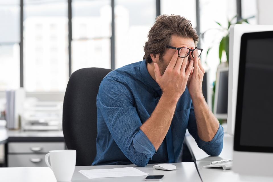 A man at a desk rubs his eyes, exhausted