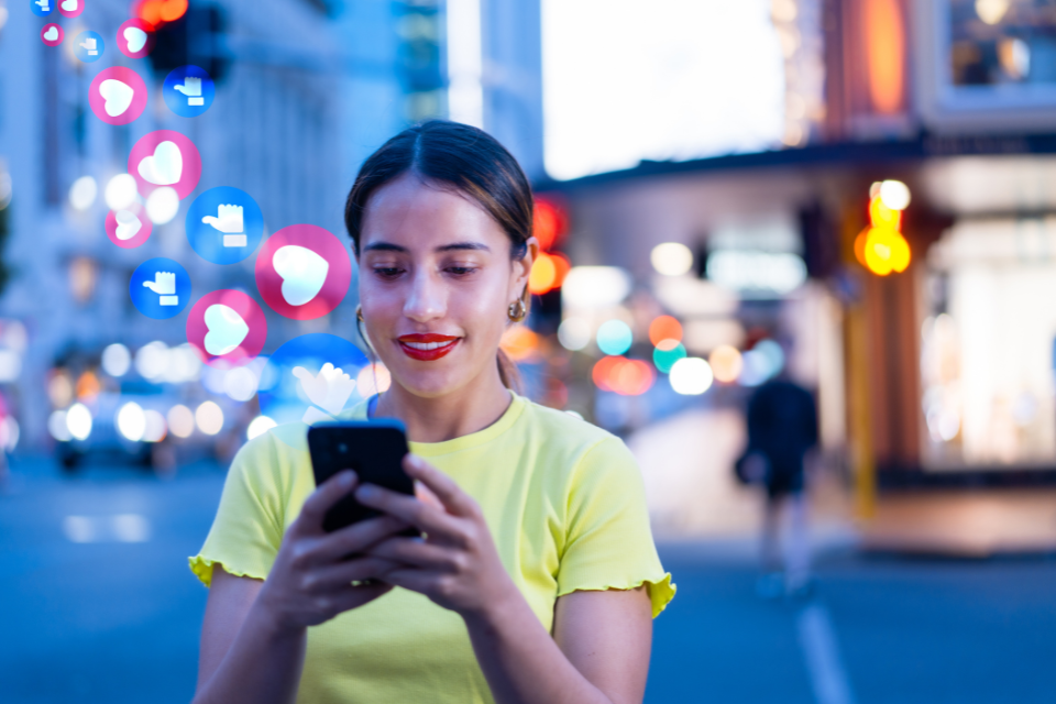 A young woman stands on the sidewalk of a city street looking at her smartphone