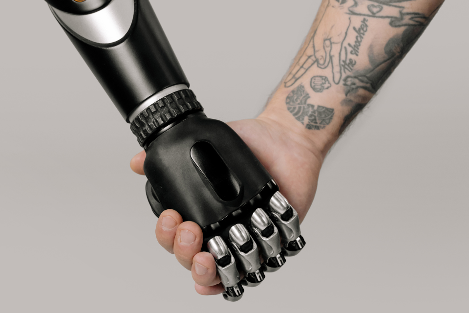A black robot arm holds hands with a tatooed human hand in the age of AI