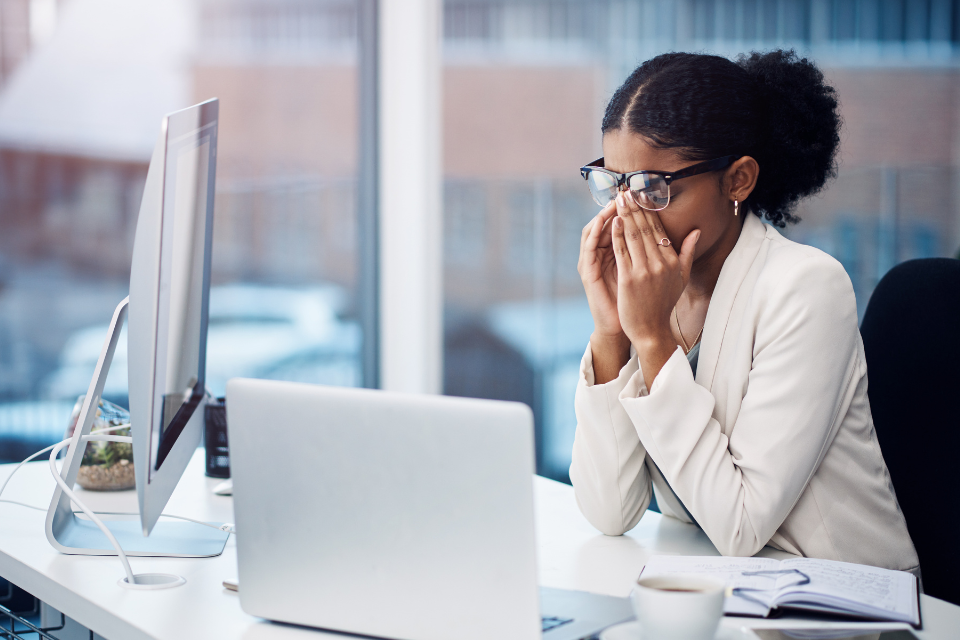 Exhausted woman rubs her eyes in front of work computer