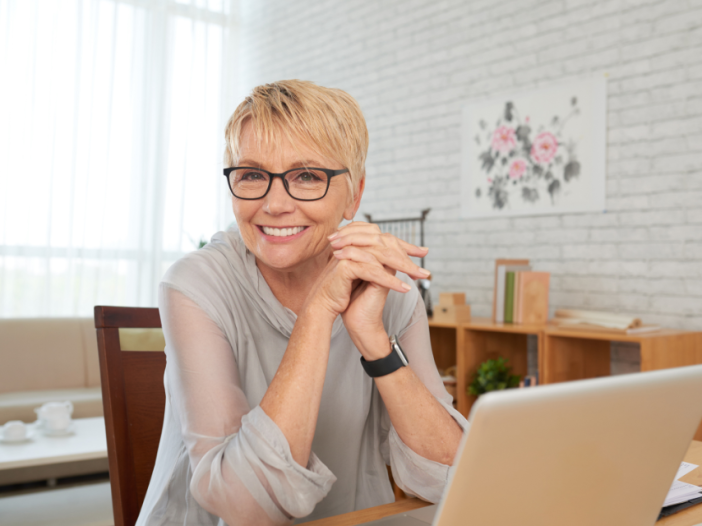 A woman in front of her laptop smiles. She is motivated by the progress principle